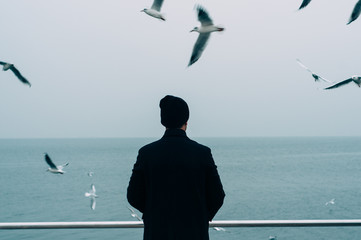 cool trendy stylish sexy handsome hipster lonely guy looking at the calm sea with seagulls back...