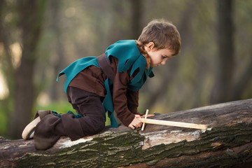 Cute little boy dressed up as a knight playing with a handmade sword while climbing a tree
