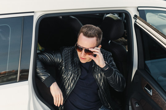 Portrait Fashionable Handsome Man in Sunglasses Sitting in rear Seat with open door. Luxury Life. Lifestyle photo. Ideal for commercial. 