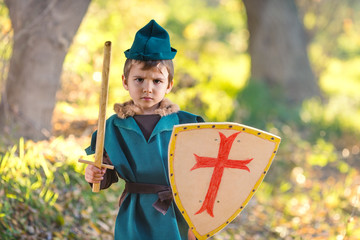 Cute little boy dressed as a knight playing with a sword and a shield in the forest