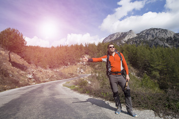 Fototapeta na wymiar Hitchhiking traveler try to stop car on the mountain road