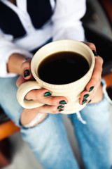 Stylish fashionable girl with a Cup of coffee and a green manicure in jeans. Fashion, care, beauty
