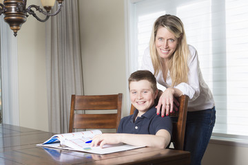 mother at a table at home helping her small son with his homework