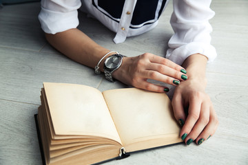 Stylish girl reading a book lying on the floor. Beautiful green manicure. Clock. A bracelet. Education, Fashion, Lifestyle
