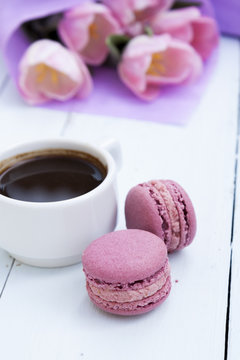 Cup of coffee and two pink macaroons on light wooden background