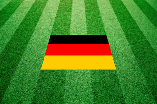 Sunny artificial green soccer or rugby grass with Germany flag background. Selective focus used.