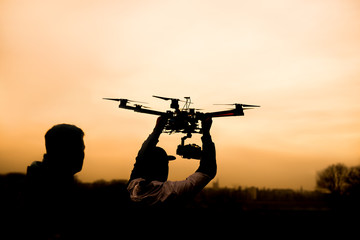 Man holding the drone, preparing for take off. Silhouette against the sunset sky. © Dusan Petkovic