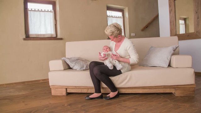 Woman and newborn sit on sofa in living room