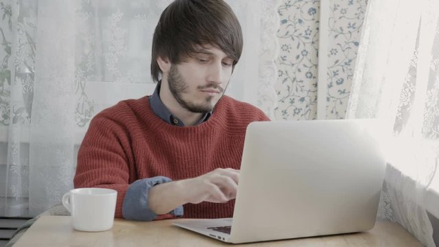 Happy Young Man Freelancer with Modern Laptop in Cafe taking Cup of Coffee