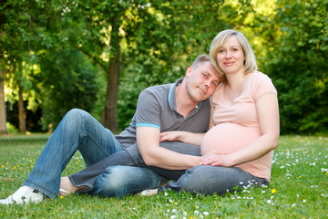 Naklejka na ściany i meble Pregnant couple resting in the park