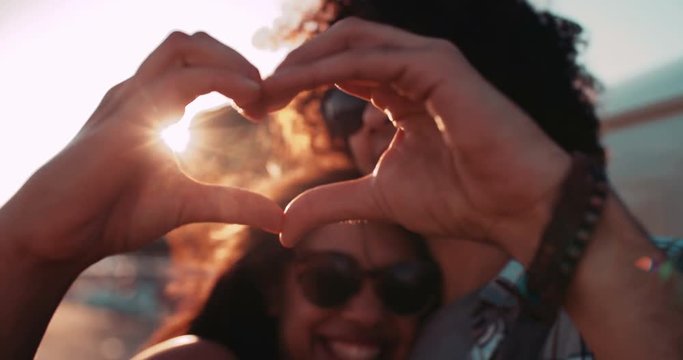 Happy young hipster couple making heart shape with hands