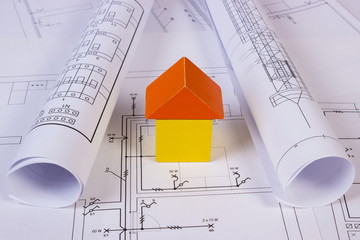 House of wooden blocks and rolls of diagrams on construction drawing of house