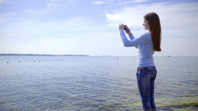 Woman stand beside a sea and take photo