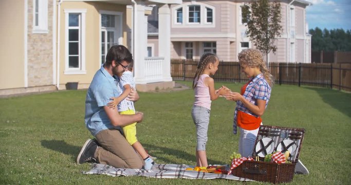 Lovely family having fun on picnic: daddy playing with son and mother playing pat-a-cake with little daughter