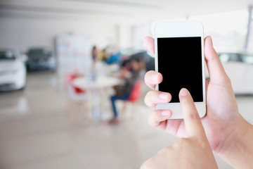 hands holding mobile phone with new cars in showroom