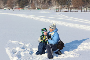 Fototapeta na wymiar The woman in a blue jacket and the little boy laughing on snow in the winter 