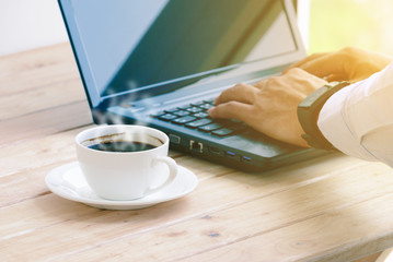 Coffee cup with closeup man typing a laptop on wooden table.