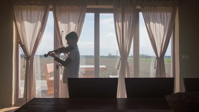 Boy silhouette playing violin in living room
