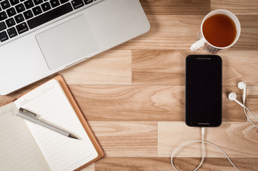 Wooden office table with laptop, notebook, pen, mobile and tea cup