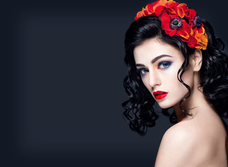 Lady in red. Beautiful woman portrait with red lips and accessories. Young girl brunette with red flowers in hair. Bright makeup and nice hairstyle.