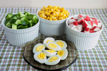 Many ingredients for the salad (sweet corn, cucumber, crab meat, quail eggs) on a light background.