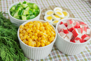 Many ingredients for the salad (sweet corn, cucumber, crab meat, quail eggs) on a light background.