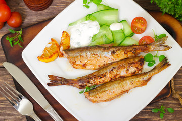Roasted sardines with a salad of cucumber and yogurt on a wooden background. Mediterranean cuisine