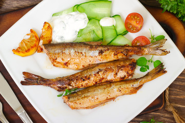 Roasted sardines with a salad of cucumber and yogurt on a wooden background. Mediterranean cuisine