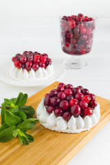 Meringue cake with cream  and cranberries decorated with mint on a white wooden background.
