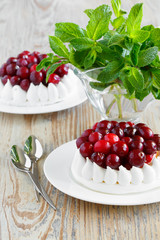 Portion of meringue cake with cream and cranberries. Fresh mint in a glass