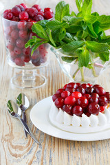 Glass of frozen cranberries. Portion of meringue cake with cream and cranberries