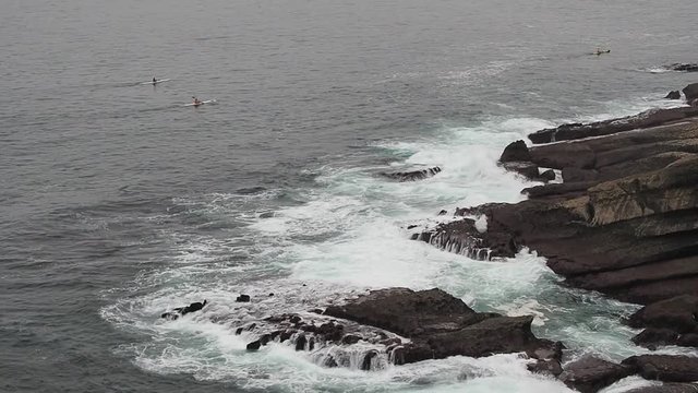 Paisaje mar&iacute;timo con piraguas en el Mar Cant&aacute;brico, remando cerca de la orilla rocosa con olas blancas, en Abril de 2016