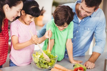 Smiling girl preparing salad with family