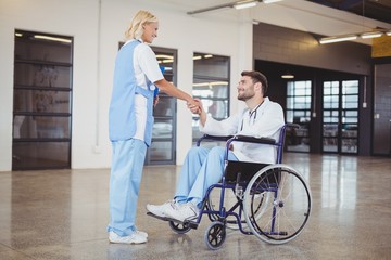 Smiling female doctor handshaking with doctor sitting on wheelchair at hospital