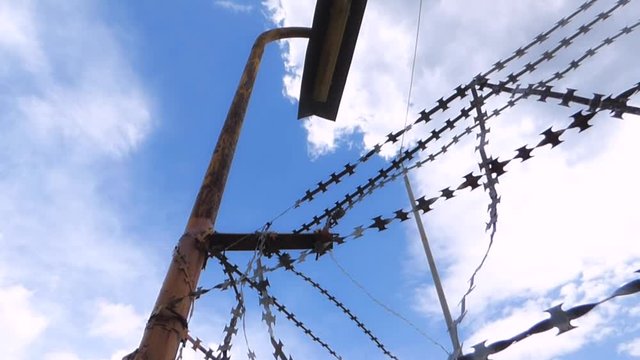 Barbed wire over the fence of the prison on the background of cloudy sky. Rusty non working lantern