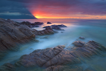 Fototapeta na wymiar Waves and rocks in motion blur on coastline at dawn