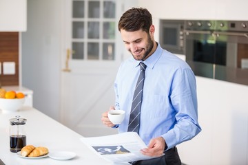 Businessman reading newspaper while drinking coffee