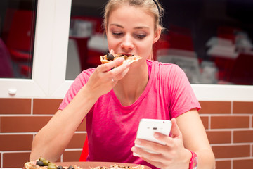 Teenager eating pizza in restaurant and chatting internet on a p