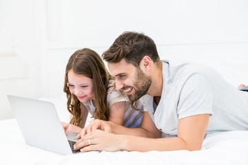 Father and daughter looking in laptop on bed © WavebreakMediaMicro