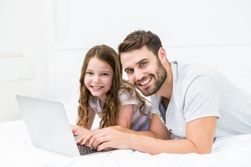 Happy father and daughter using laptop on bed