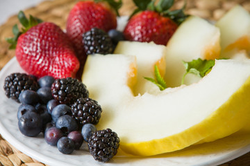 A white plate with fresh organic fruit. Summer snack. Blueberries, melon, strawberries with mint. Healthy food for healthy life.