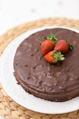 Homemade dark chocolate cake decorated with cocoa and fresh organic strawberries on top served on a white plate and straw tablemat. Delicious party cake fo celebration or holidays.