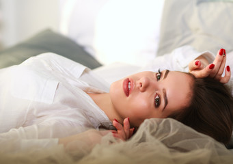 Fototapeta na wymiar Beautiful thoughtful girl lying in bed on background of sunlight