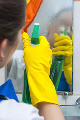 Woman in yellow gloves with spray and rag