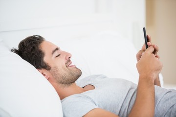 Close-up of young man smiling while using mobile phone on bed at home