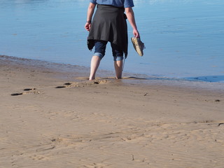 Persona caminando con los pies hundidos en la arena de la playa  hasta los tobillos hacia el agua del mar azul, en primavera de 2016 Santander, Espa&ntilde;a