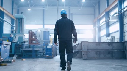 Follow footage of factory worker in a hard hat that is walking through industrial facilities. Shot on RED Cinema Camera. - Powered by Adobe