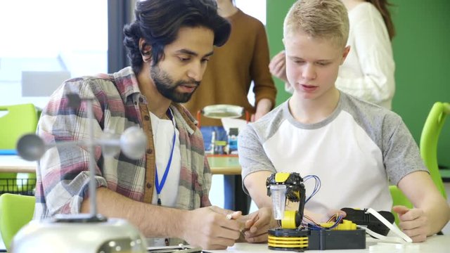 Young, male teacher helping his student build a robotic arm.