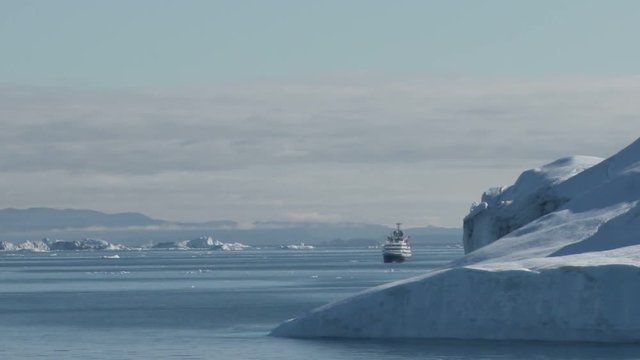 View of the icebergs of Disko Bay, Ilulissat, Greenland with a small cruise ship in the background