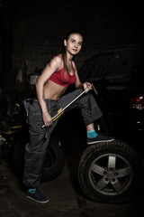 Fototapeta na wymiar sexy girl mechanic sitting on a tire holding a wrench in his hand. colorless life concept